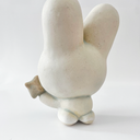 Small white ceramic sculpture of a bunny character with a calm, closed eye expression. It has a large head and a tiny body, holding a star.