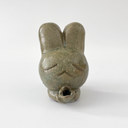 Small sage green ceramic sculpture of a bunny character with a giant head and a tiny body. It holds out a small tulip like flower in its hands.