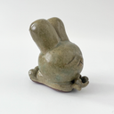Small sage green ceramic sculpture of a bunny character with a giant head and a tiny body. It holds out a small tulip like flower in its hands.