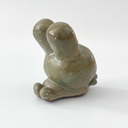 Small sage green ceramic sculpture of a bunny character with a giant head and a tiny body. It holds out a small tulip like flower in its hands.
