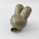 Small sage green ceramic sculpture of a bunny character with a giant head and a tiny body. It holds out a small tulip like flower in its hands.