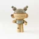 Ceramic statue of a character with closed eyes, a small dress, ear cuffs and their hair up in space-like buns. On their arm is a small caterpillar and on their knee is a bandaid. 