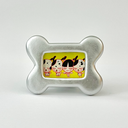 Small painting of 3 white dogs with black spots standing in a line with a girl, they all have the same expression and are the same height. Piece is in a silver bone shaped frame.