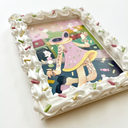 Painting of a green haired cartoon character wearing a pink dress and walking down a street while holding 2 sticks of dango, with tiny bunnies dancing on them. Piece is framed in a deco-den frosting themed frame.