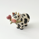 Ceramic figurine with a spotted clay finish of a cow with a flower in its mouth.
