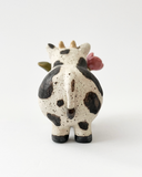 Ceramic figurine with a spotted clay finish of a cow with a flower in its mouth.