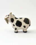 Ceramic figurine with a spotted clay finish of a cow with a flower in its mouth.