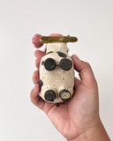 Ceramic figurine with a spotted clay finish of a cow with a flower in its mouth.