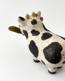 Ceramic figurine with a spotted clay finish of a cow with a flower in its mouth.