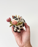 Hand holding a small cow figurine with a white background
