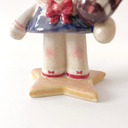 Ceramic figure of a girl with pink, anime-like hair, a sailor outfit and holding a cute black cat head. She stands on a star shaped base.
