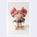 Photo print of a ceramic figure of a girl with pink, anime-like hair, a sailor outfit and holding a cute black cat head. She stands on a star shaped base.
