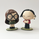 Ceramic sculpture of a stylized Daria from the show Daria - a girl with long brown hair, large glasses, a green coat and a black skirt with boots. She stands on a bullseye colored green, next to her companion Jane Lane.