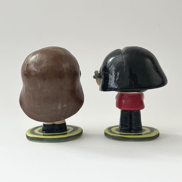 Ceramic sculpture of a stylized Daria from the show Daria - a girl with long brown hair, large glasses, a green coat and a black skirt with boots. She stands on a bullseye colored green, next to her companion Jane Lane.
