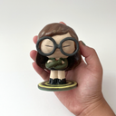Ceramic sculpture of a stylized Daria from the show Daria - a girl with long brown hair, large glasses, a green coat and a black skirt with boots. She stands on a bullseye colored green.