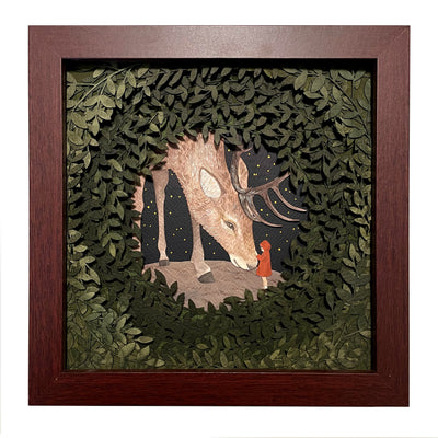 Layered cut paper diorama style sculpture in an open wooden frame, with many layers of leaves revealing a small scene of a red cloaked child petting the face of a very large Elk, which bows its head to the child.