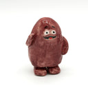 A small hand-painted ceramic figurine of a round, reddish-brown character with a white face, black eyes, and a red mouth, standing on a white background.