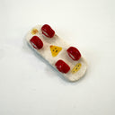 Underside of a mini ceramic skateboard, with red wheels and a yellow onigiri design.