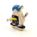 A hand-painted ceramic figurine of an onigiri character riding a skateboard, wearing a blue cap with yellow color accents, set against a plain white background.