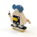A hand-painted ceramic figurine of an onigiri character riding a skateboard, wearing a blue cap with yellow color accents, set against a plain white background.