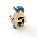 A miniature ceramic onigiri character, walking with its arms in full stride. It wears a blue and yellow cap, has yellow sleeves, yellow and blue sneakers and stickers on the side of its body.