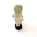 A miniature ceramic onigiri character, riding a skateboard, with its arms in full stride. It wears a green cap, has blue sleeves, blue and green sneakers and stickers on the side of its body.