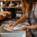 Person in a bakery doing dishes with a sponge shaped like and designed as a croissant.