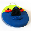 Sculpture of a flat clay mask with 3D eyes, nose and lips. It is half fluorescent yellow and half dark blue. It has red eyes and eyebrows and hangs from a chain.