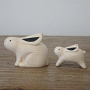 Two white wood figurines of rabbits, one is slightly larger than the other.