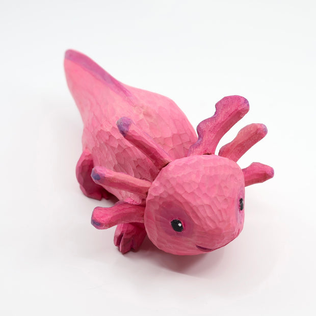 Whittled wooden sculpture of a pink, smiling axolotl. 