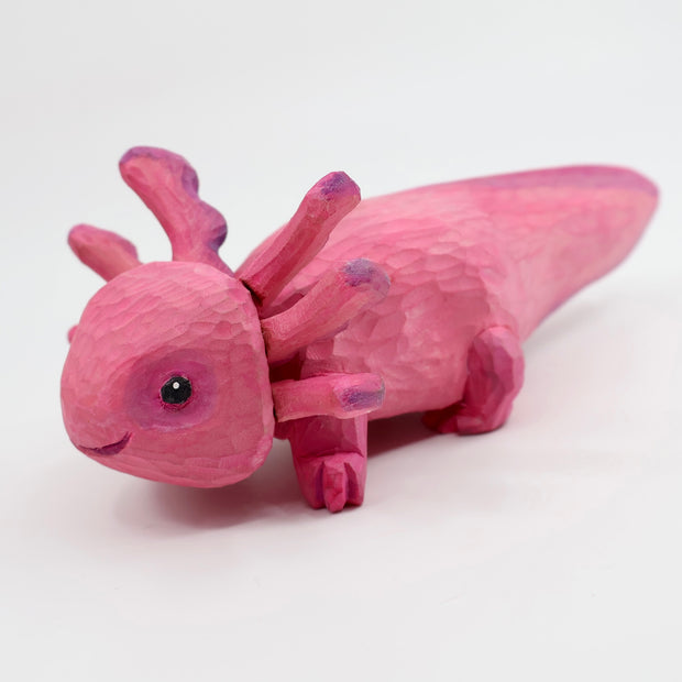 Whittled wooden sculpture of a pink, smiling axolotl.