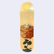 Light yellowish orange skate deck with an illustration of a very large flower with many dark orange petals, stacked atop on another like a fluffy collar. In the center of the flower, a small head emerges. Flower is attached to a dark green leafed stem and a yellow sun shines overhead.