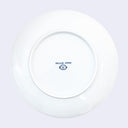 Back of a white ceramic plate with a small signature in blue by Felicia Chiao with a very small cartoon head smiling.
