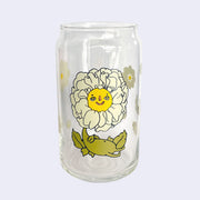 Glass cup with a flat base and slightly inward lip. Features a graphic of a cartoon style white camellia, sitting with a smiling face and a chubby green body made out of stems and leaves. Around the rest of the glass are white flowers.