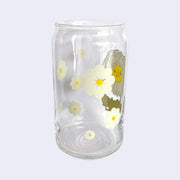 Glass cup with a flat base and slightly inward lip. Features a graphic of a cartoon style white camellia, sitting with a smiling face and a chubby green body made out of stems and leaves. Around the rest of the glass are white flowers. Side view.