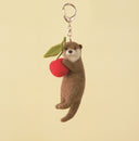 A needle felting of an other holding a cherry, attached to a keychain.