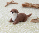 Needle felted otter, laying on its stomach with its head raised and a cute expression.