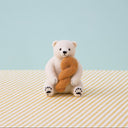 A needle felted polar bear, sitting with a large piece of twisted bread (or a donut twist) in its arms.