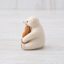 A needle felted polar bear, sitting with a large piece of twisted bread (or a donut twist) in its arms.