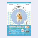 Packaging for a needle felting kit of a polar bear with a croissant, attached to a gold hardware keychain.