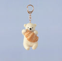 A needle felting of a polar bear with a croissant, attached to a gold hardware keychain.