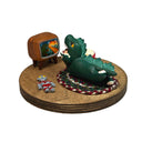 Sculpture of a child in a green kaiju costume laying on a braided carpet and watching a TV, with a bowl of popcorn and a toy robot figurine nearby. A monster movie is on the TV.