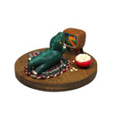 Sculpture of a child in a green kaiju costume laying on a braided carpet and watching a TV, with a bowl of popcorn and a toy robot figurine nearby. A monster movie is on the TV.