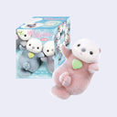 Small flocked figurine of a brown and white sea otter, with its hands extended out and a green shell on its stomach. It sits in front of its product packaging.