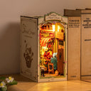 Miniature model of a floral shop with illuminated interior, displayed on a wooden surface.