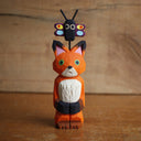 Painted whittled wooden sculpture of a fox with a surprised look on its face. It stands on its hind legs with its hand together. Atop its head is a small butterfly.