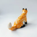 Glossy ceramic sculpture of an orange fox, with carved out poppy flower design on its back and gold colored detailing on its paws and cheeks.