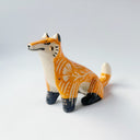 Glossy ceramic sculpture of an orange fox, with carved out poppy flower design on its back and gold colored detailing on its paws and cheeks.