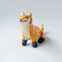 Glossy ceramic sculpture of an orange fox, with carved out poppy flower design on its back and gold colored detailing on its paws and cheeks.