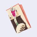 Rectangular cream colored towel with a pink outline and imagery of a pink embroidered fox, jumping down into burrows that can be seen from the side, Each burrow has small seeds stored and small green mice. 